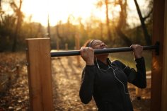 Frau die einen Klimmzug an einer Stange im Wald macht