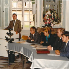 Vier Leute sitzen an einem halbrunden Tisch und ein Mann steht an einem Rednerpult