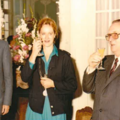 Zwei Männer und eine Frau halten ein Glas in der Hand und strecken es nach oben 