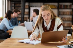 Eine Frau sitzt an einem Tisch auf dem Bücher und Schreibutensilien liegen