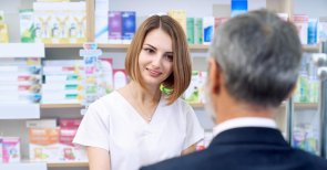 Ein Mann steht vor einer Frau, die weiß gekleidet ist und hinter ihr stehen viele unterschiedliche Medikamente