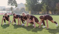 Einige junge Frauen die gleiche Kleidung tragen machen Übungen auf dem Rasen
