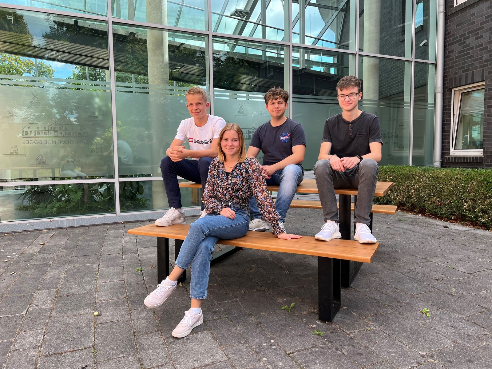 Vier junge Menschen sitzen auf einer Bank vor einem Gebäude
