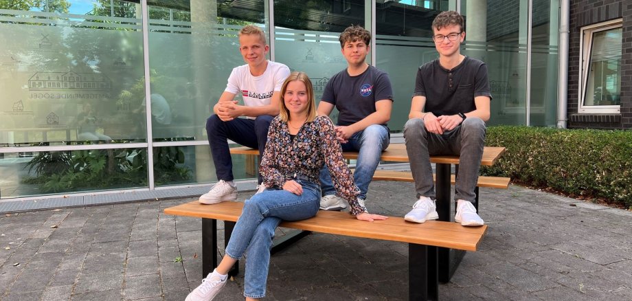 Vier junge Menschen sitzen auf einer Bank vor einem Gebäude
