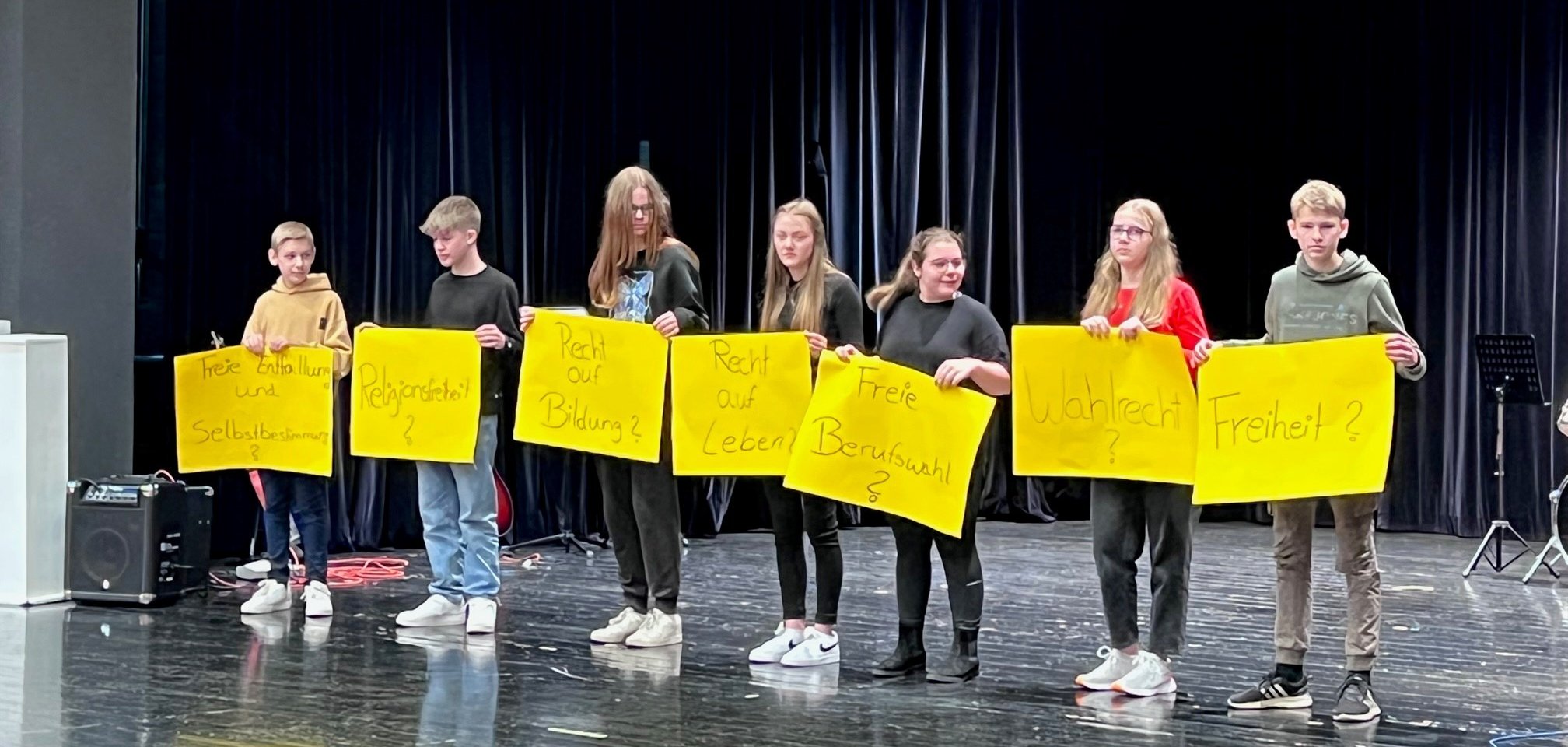 Jugendliche stehen auf einer Bühne und halten Plakate hoch 