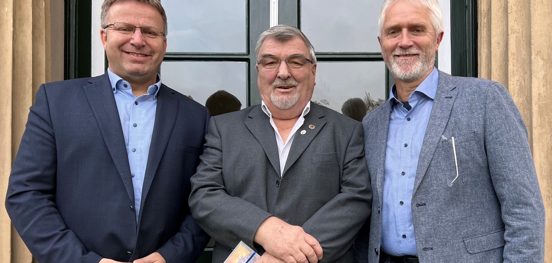 Ein Bild mit drei Personen vor dem Rathaus