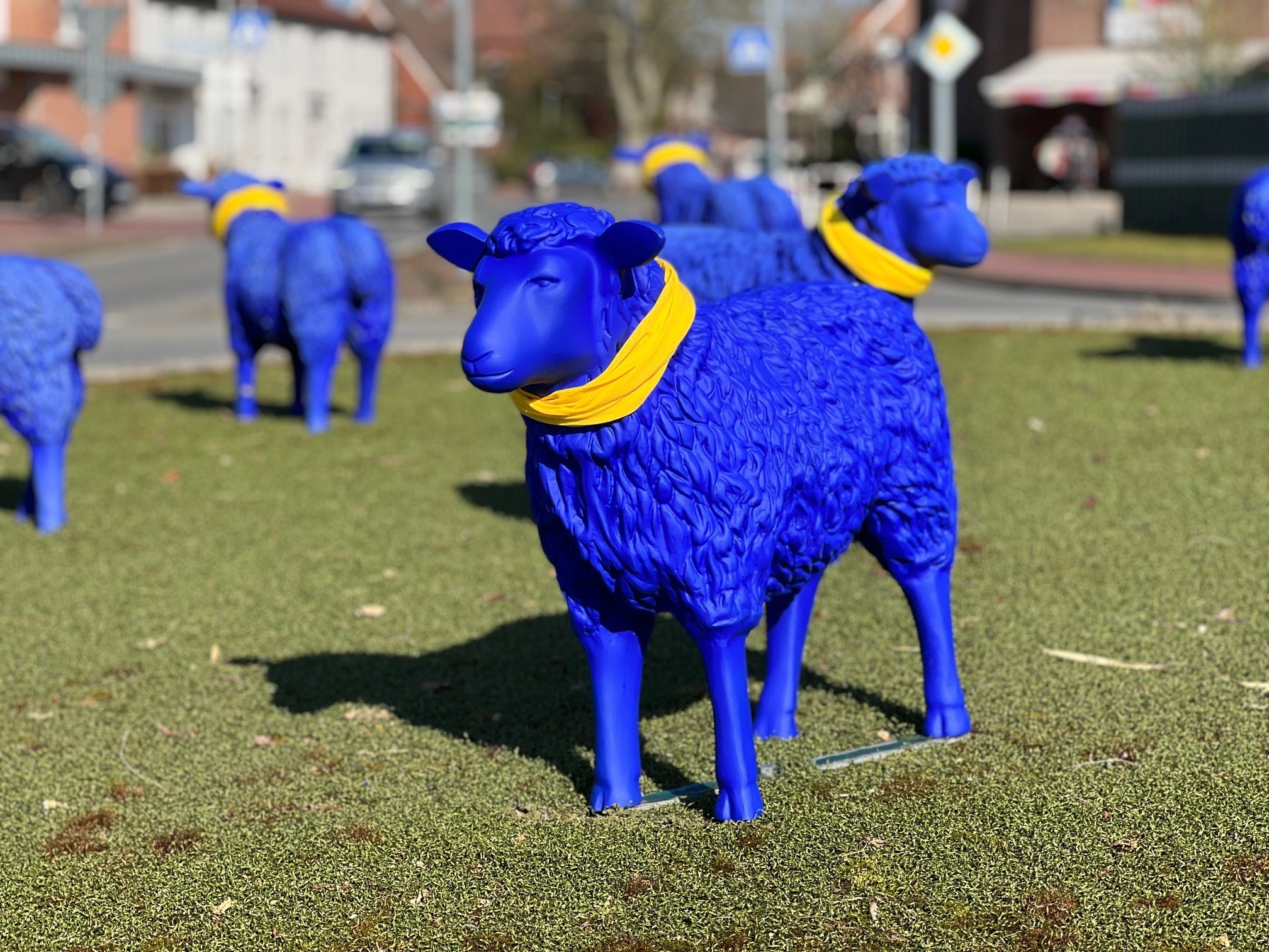 Blaue Dekorationsschafe mit einem gelben Tuch um den Hals auf einer Verkehrsinsel