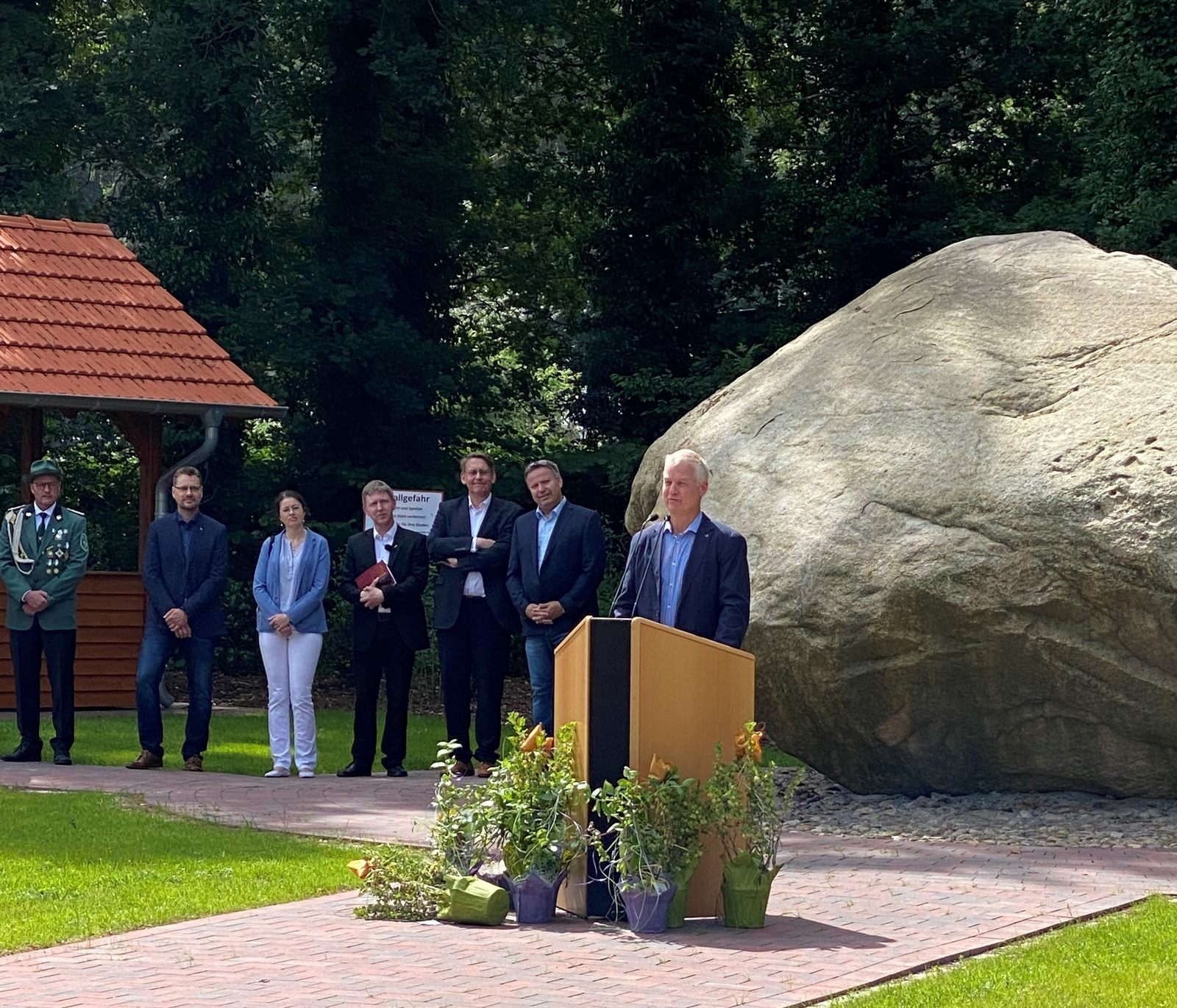 Ein Mann steht vor einem Rednerpult vor einem sehr großen Stein 