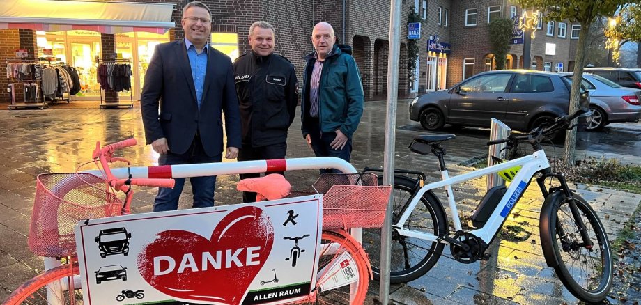 Zwei Männer stehen neben einem Polizisten und vor Ihnen steht ein Fahrrad mit einem Plakat auf dem Danke steht 