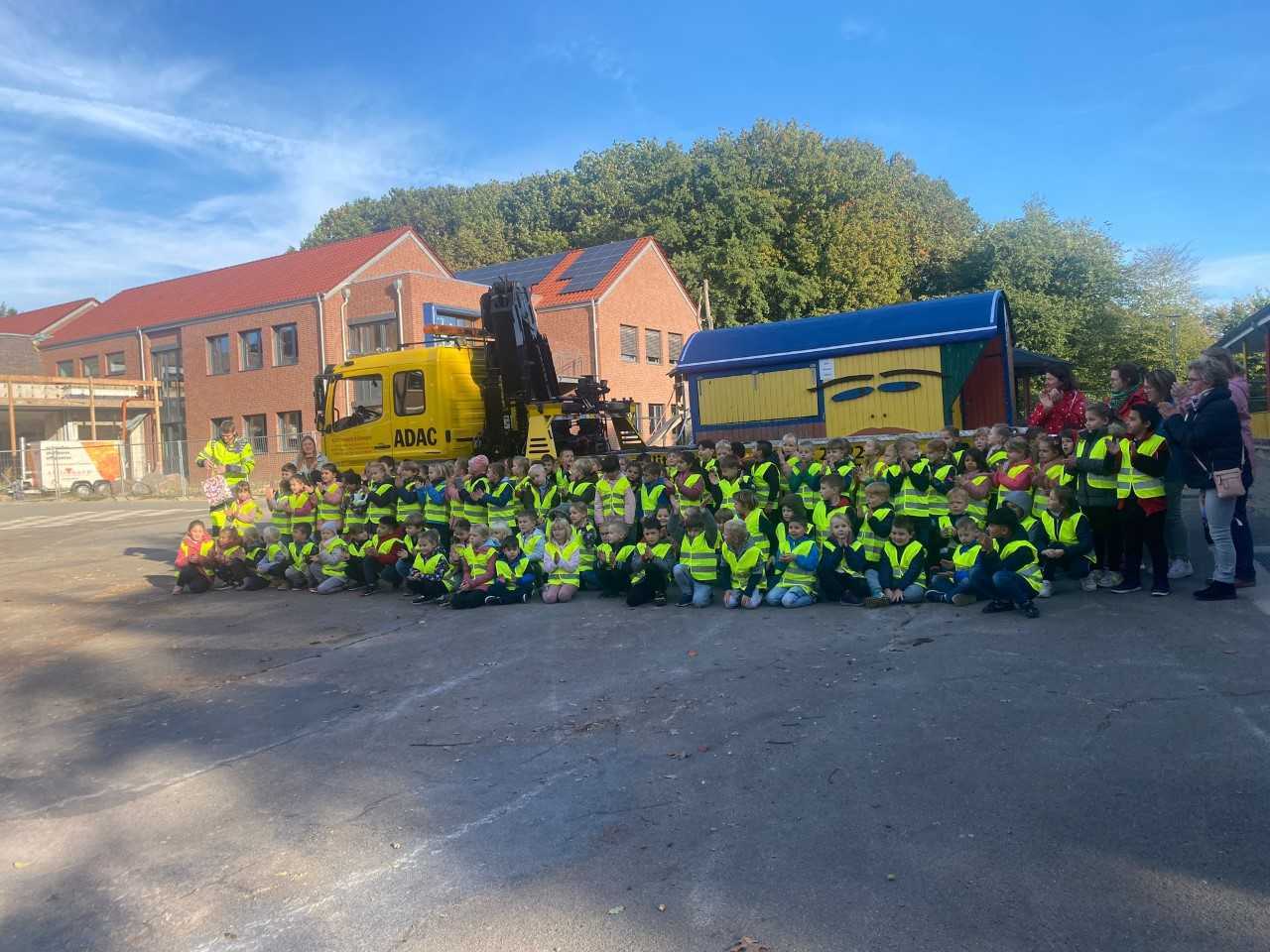 Viele Kinder tragen eine gelbe Warnweste und stehen vor einem ADAC LKW 