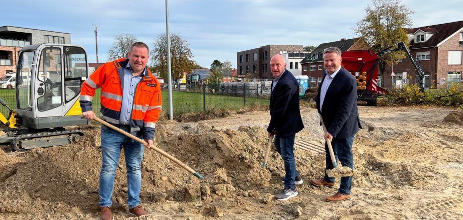 Drei Männer mit einer Schaufel in der Hand die vor einem Sandhaufen stehen 