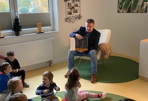 Mann hält ein buch in der Hand vor ihm sitzen viele kleine Kinder 
