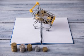 Aufgeschlagener Notizblock mit einem Miniatur Einkaufswagen in dem Kleingeld liegt